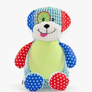 May include: A soft dog toy with a light blue textured body, red and blue polka dot details, and a green belly. The dog has a smiling face with a pink tongue and a green eye patch. A colourful and cute stuffed animal.