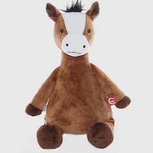May include: A soft toy horse in brown, white, and black. The horse has a white face with black eyes and a black mane. The toy is sitting with its arms and legs extended. A red tag is attached to the toy's arm.