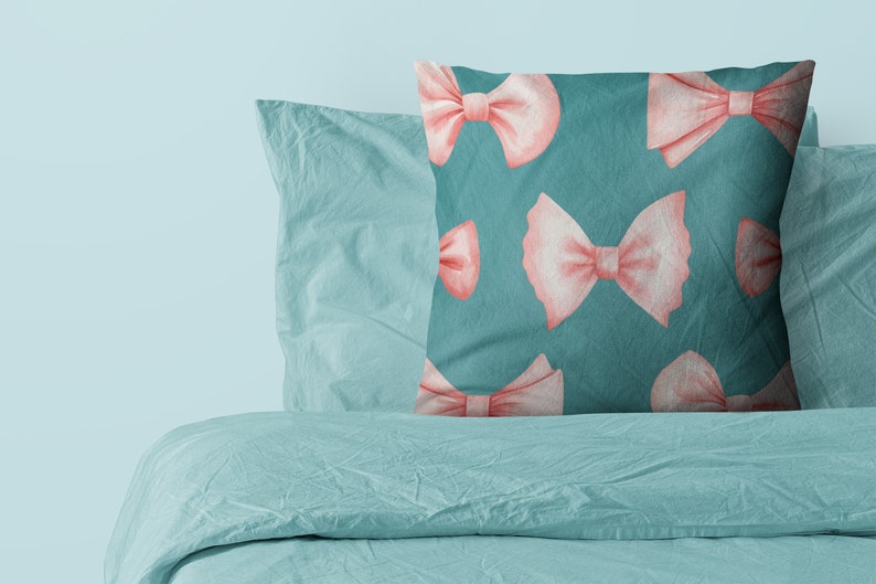 K&ouml;nnte beinhalten: Ein blaues Kissen mit einem Muster aus rosa Schleifen. Das Kissen liegt auf einem Bett mit einem blauen Bettbezug.