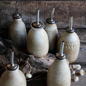 May include: Six ceramic olive oil bottles with stainless steel spouts. The bottles are speckled with brown and white glaze and have a rustic look.