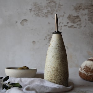 Może przedstawiać: Biała ceramiczna butelka do oleju i octu w białe plamki z srebrnym dzióbkiem i czarnym pierścieniem wokół górnej części.