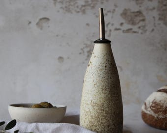 May include: A speckled white ceramic oil and vinegar bottle with a silver spout and a black ring around the top.