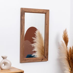 May include: A rectangular wooden framed mirror with a brown wood frame. The mirror reflects a brown and white abstract design.