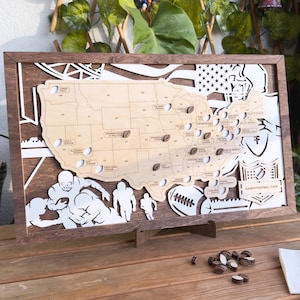 May include: Wooden United States map with football stadium locations and football-shaped markers. The map is framed in dark brown wood, with white cut-out football players and a football. The text "DAVID'S FOOTBALL TOUR" is visible.