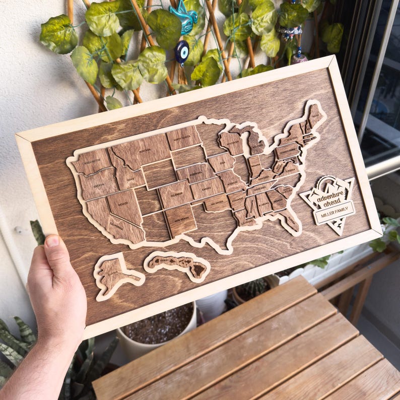 May include: A wooden map of the United States with each state outlined and labeled. The map is framed in a light wood frame. The text "adventure ahead" and "Miller Family" is engraved on the map.