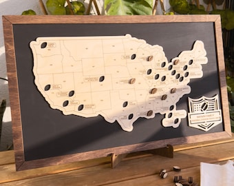May include: A wooden map of the United States with a black frame and a stand. The map has holes for placing small wooden footballs to mark locations. The map also has the text "Brown Family Football Stadium Map" on the right side.