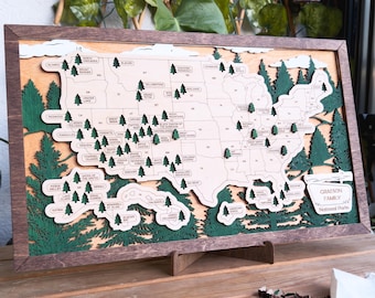 May include: A wooden map of the United States with green wooden trees representing national parks. The map is framed in dark wood and has a stand. The text "Graeson Family National Parks" is at the bottom right corner of the map.