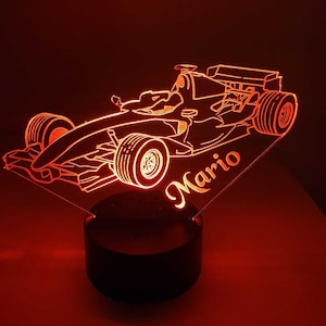 Può includere: Una luce notturna a LED rossa stampata in 3D a forma di auto da corsa con il nome Mario stampato sul lato.