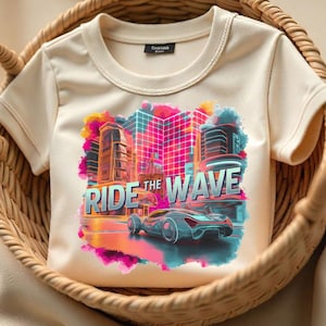 Puede incluir: Una camiseta de color crema con un estampado gráfico de una ciudad futurista con un coche conduciendo por las calles. El texto "RIDE THE WAVE" está impreso en letras negritas en la camiseta.