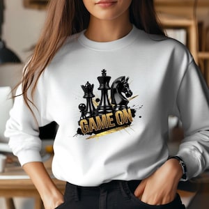 May include: White sweatshirt with a black and gold design featuring chess pieces and the text "GAME ON".