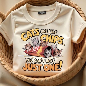 Puede incluir: Una camiseta de color crema con un gráfico de gatos en una bolsa de patatas fritas. El texto dice "Los gatos son como las patatas fritas... No puedes tener solo una!"