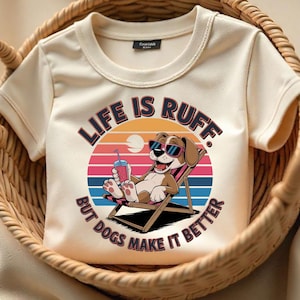 Könnte beinhalten: Ein weißes T-Shirt mit einem Cartoon-Hund, der eine Sonnenbrille trägt und ein Getränk hält. Der Text auf dem Shirt lautet "Life is Ruff. But dogs make it better."