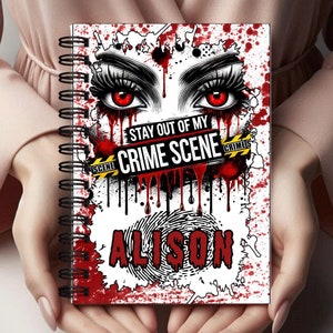 Puede incluir: Una libreta de espiral blanca con un diseño rojo, blanco y negro. El diseño presenta un par de ojos rojos con pestañas negras, salpicaduras de sangre y una cinta de la escena del crimen amarilla y negra que dice "Stay Out of My Crime Scene". El nombre "Alison" está escrito en letras rojas sobre una huella digital blanca.