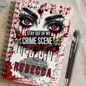 Könnte beinhalten: Ein spiralgebundenes Notizbuch mit einer Grafik aus roten Augen mit langen Wimpern, roten Blutspritzern und gelbem Tatortband mit dem Text STAY OUT OF MY CRIME SCENE. Der Name REBECCA ist in Rot unter einem Fingerabdruck abgebildet.