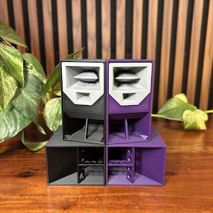 May include: A set of four miniature speaker enclosures arranged in a square formation. Two are black and two are purple, each featuring a light grey horn-loaded tweeter section at the top and a rectangular woofer opening at the bottom.