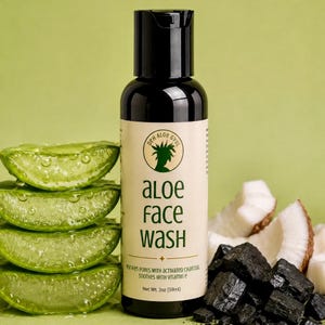 May include: A black plastic bottle of face wash with a beige label featuring the text DEH ALOE GYUL, ALOE FACE WASH, PURIFIES PORES WITH ACTIVATED CHARCOAL, SOOTHES WITH VITAMIN E, and Net Wt. 2oz. It is surrounded by aloe vera slices and charcoal.