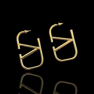 Puede incluir: Un par de pendientes de aro dorados con un dise&ntilde;o geom&eacute;trico. Los pendientes est&aacute;n hechos de un metal grueso y resistente y tienen un acabado pulido.