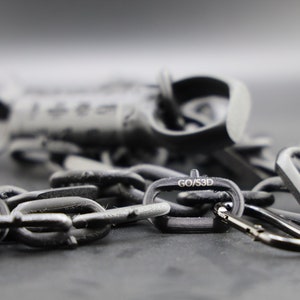 May include: A black chain with a black carabiner clip and a black metal tag that says "GO/S3D".