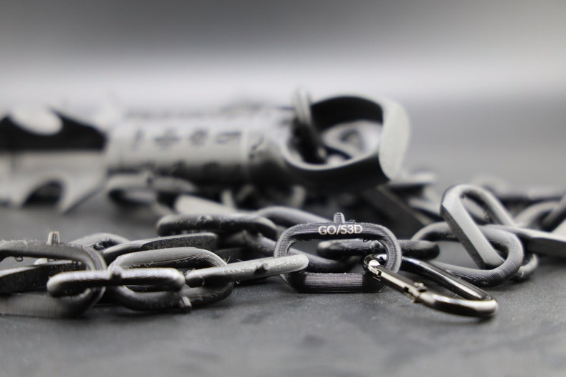 May include: A black chain with a black carabiner clip and a black metal tag that says "GO/S3D".