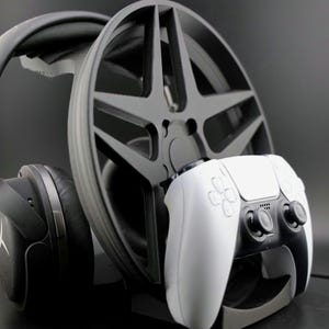 May include: A black gaming headset and a white PlayStation 5 controller are displayed on a black stand with a black wheel design.