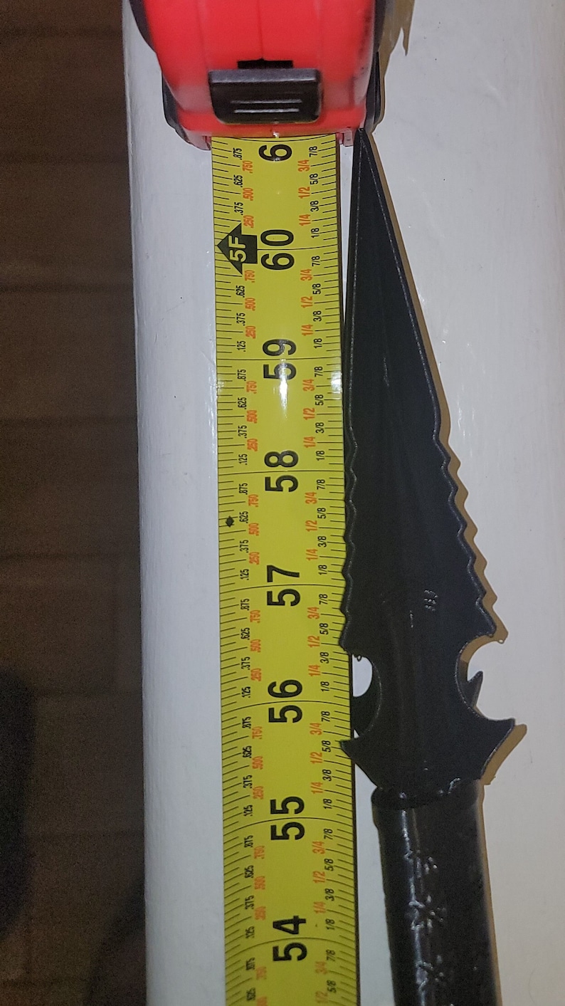 May include: A black metal knife with a serrated blade and a handle with a textured design. The knife is measured against a yellow tape measure that reads 54 to 60 inches.