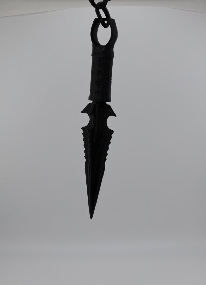 May include: A black metal dagger with a serrated blade and a ring at the top. The dagger is hanging from a chain.