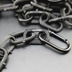 May include: A black chain with a black carabiner clip. The chain has a label that reads "GO/S3D".