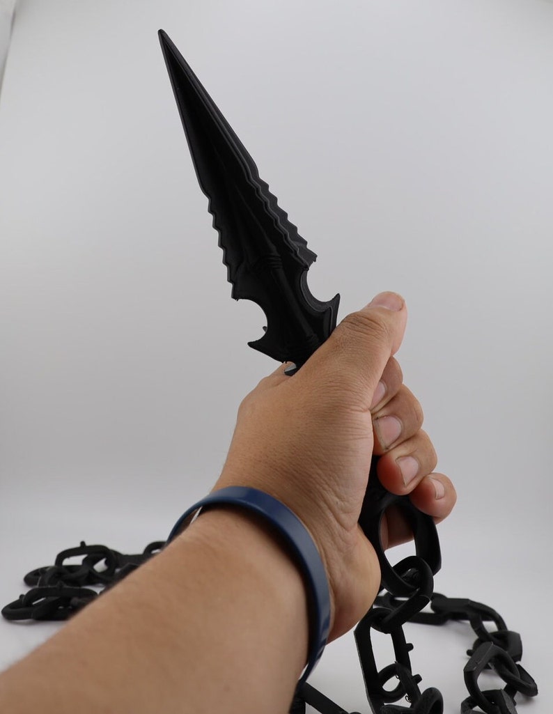 May include: A black plastic dagger with a serrated blade and a chain attached to the handle.