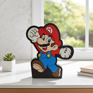 May include: A colourful figurine of Mario, a popular video game character, in a jumping pose. The figurine features a red hat with a white "M", blue overalls, and a black base. The figure is approximately 20 cm tall.