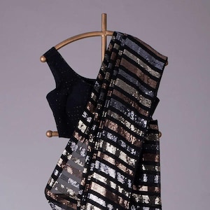 May include: A black saree with silver and gold sequins in a horizontal striped pattern. The saree is draped over a hanger.