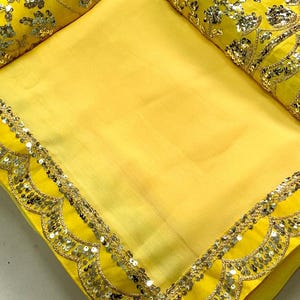 Pu&ograve; includere: Un sari giallo brillante con un bordo smerlato impreziosito da paillettes argentate e finiture dorate. Il sari ha un pezzo di camicetta giallo abbinato con intricati ricami floreali e dettagli di paillettes. Il tessuto sembra essere un materiale leggero e fluido.