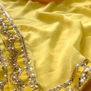 Pu&ograve; includere: Un tessuto giallo vivace con un bordo decorato. Il bordo presenta un design smerlato ornato di paillettes argentate. Il tessuto &egrave; drappeggiato, mostrando la sua texture fluida e il colore solare. Adatto per abbigliamento o decorazioni.