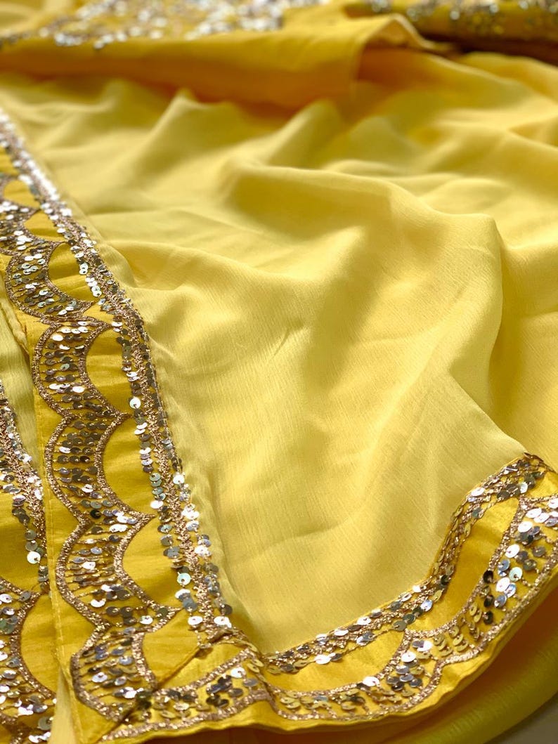 Pu&ograve; includere: Un tessuto giallo vivace con un bordo decorato. Il bordo presenta un design smerlato ornato di paillettes argentate. Il tessuto &egrave; drappeggiato, mostrando la sua texture fluida e il colore solare. Adatto per abbigliamento o decorazioni.