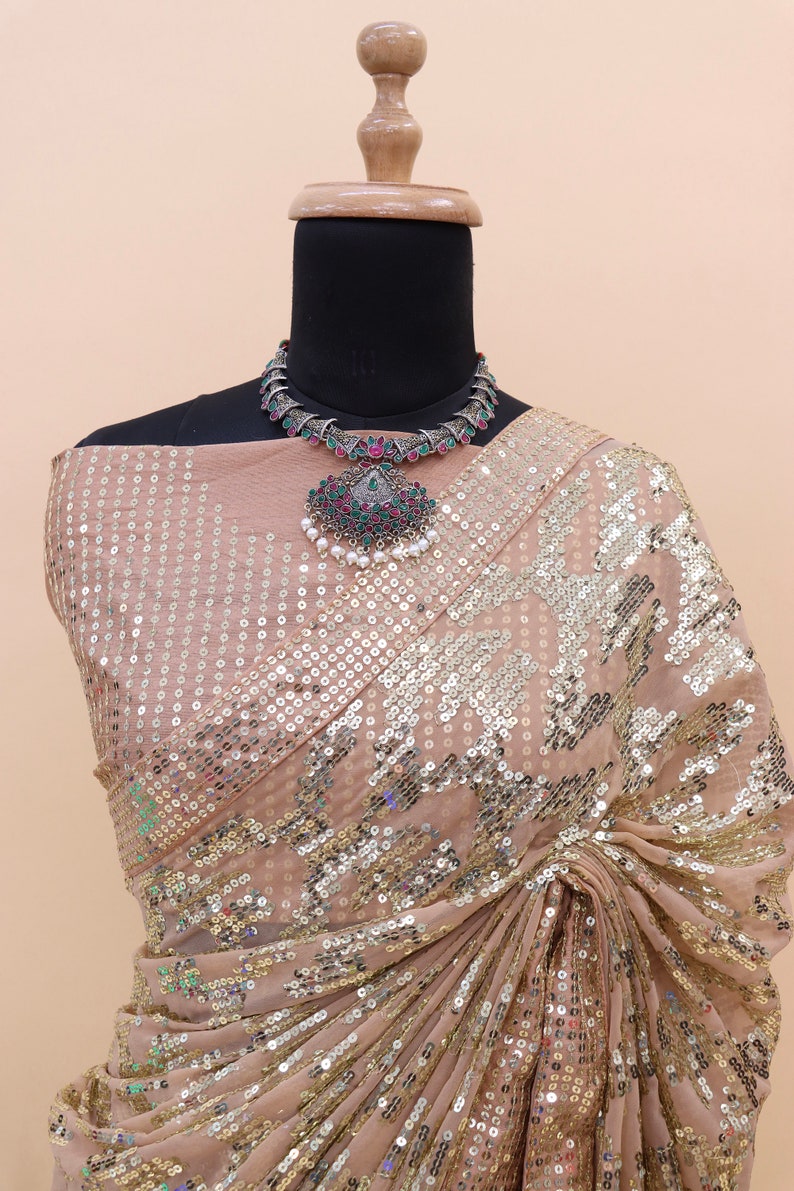 Może przedstawiać: Beige saree z cekinami i srebrną i zieloną naszyjnikiem z klejnotami. Saree jest udrapowane na manekinie.