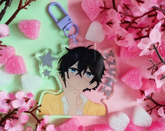 May include: A clear acrylic keychain featuring an anime character with black hair and blue eyes, the name "IZUMI" is printed on the right side. The keychain has a purple clasp and is surrounded by pink heart-shaped candies and pink flowers.