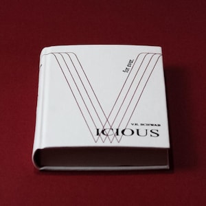 May include: A hardcover book titled "Vicious" by V.E. Schwab. The book has a white cover with a stylized "V" design in burgundy lines. The words "for ever." are printed vertically on the cover.