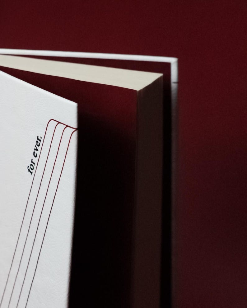 May include: Close-up of a book with white pages and a burgundy cover. The text "for ever." is printed vertically on the left side of the open book. The pages are cream-colored, and the background is a deep burgundy.