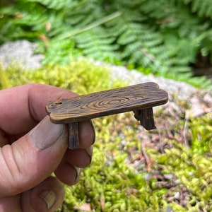 May include: A miniature wooden bench with a rustic brown finish and a wood grain pattern. The bench has four legs and is made of a sturdy material.