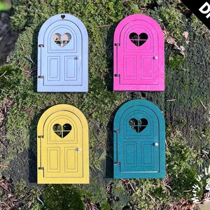 May include: DIY kit for four fairy doors, each with a heart-shaped window. The doors are painted in light blue, pink, yellow, and teal.
