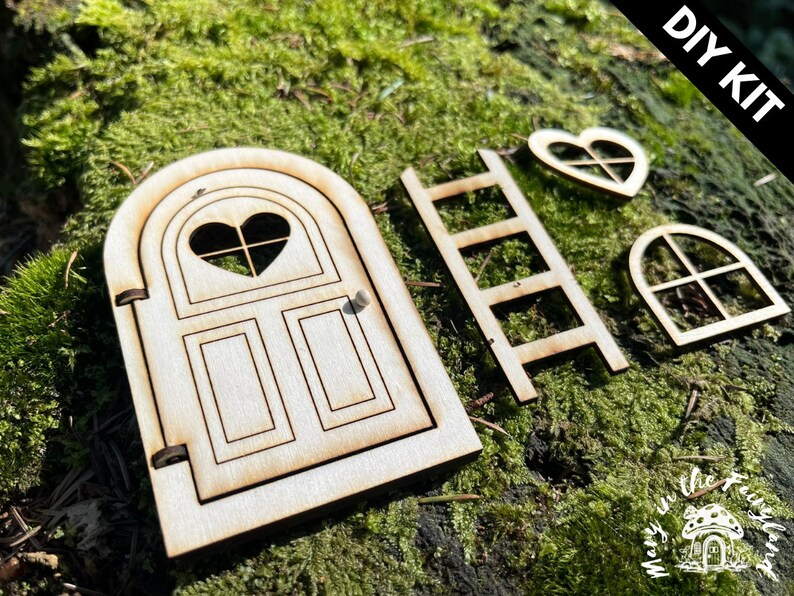 May include: DIY kit for a fairy door, featuring a wooden door with a heart-shaped window, a ladder, a heart-shaped window, and a rectangular window. The kit is made of unfinished wood and is ready to be painted or stained.