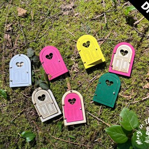 May include: DIY kit of six unfinished wooden fairy doors with heart-shaped windows. The doors are painted in various colors, including pink, blue, yellow, green, and white.