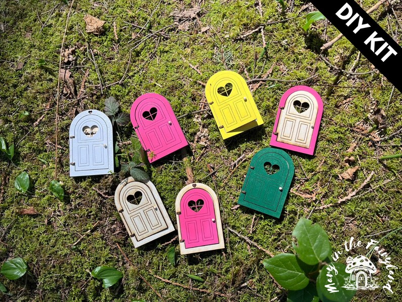 May include: DIY kit of six unfinished wooden fairy doors with heart-shaped windows. The doors are painted in various colors, including pink, blue, yellow, green, and white.