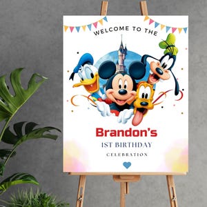 May include: A rectangular birthday sign featuring Mickey Mouse, Donald Duck, Goofy, and Pluto in front of a castle. The text reads WELCOME TO THE, Brandon's, 1ST BIRTHDAY, CELEBRATION, with colorful bunting at the top and a small blue heart at the bottom.