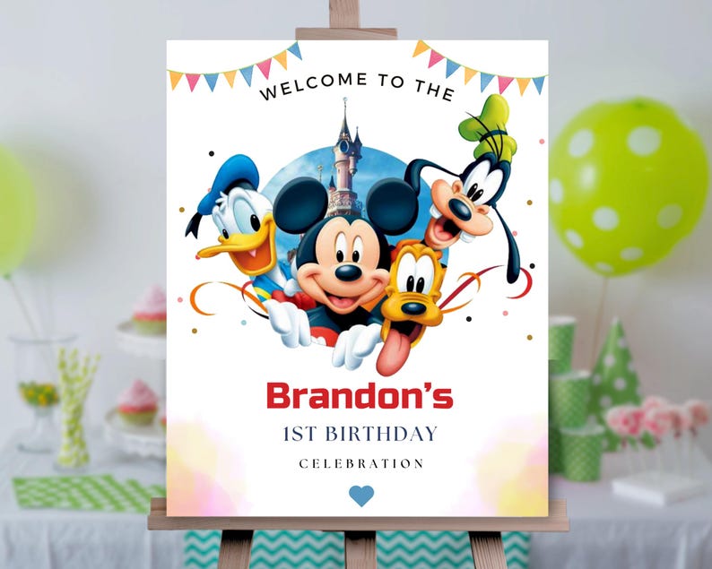 May include: A rectangular birthday sign featuring Mickey Mouse, Donald Duck, Goofy, and Pluto in front of a castle. The text reads WELCOME TO THE, Brandon's, 1ST BIRTHDAY, CELEBRATION, with colorful bunting at the top and a small blue heart at the bottom.
