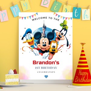 May include: A rectangular birthday sign featuring Mickey Mouse, Donald Duck, Goofy, and Pluto in front of a castle. The text reads WELCOME TO THE, Brandon's, 1ST BIRTHDAY, and CELEBRATION, with colorful bunting at the top and a small blue heart at the bottom.