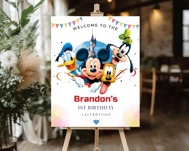 May include: A rectangular sign on a wooden easel featuring colorful bunting at the top and the text WELCOME TO THE. Below, illustrations of Mickey Mouse, Donald Duck, Goofy, and Pluto appear in front of a castle. Text reads Brandon's 1ST BIRTHDAY CELEBRATION.