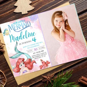 Puede incluir: Una invitaci&oacute;n de cumplea&ntilde;os con el texto "Our Little Mermaid Madeline is turning 4." La invitaci&oacute;n incluye una ilustraci&oacute;n de Ariel, una sirena, y una foto de una ni&ntilde;a con un vestido rosa. La invitaci&oacute;n est&aacute; sobre una superficie de madera.