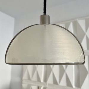 May include: A modern pendant light with a semi-circular, frosted glass shade. The shade is framed by a thin, dark metal band and suspended from a black cord. The fixture has a minimalist design, suitable for various interior styles.