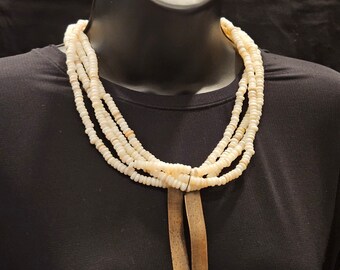 May include: A white beaded necklace with a long, rectangular pendant made of metal. The necklace is layered and has a simple, elegant design.