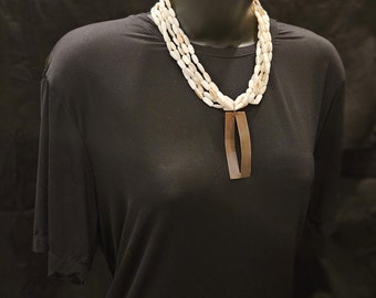 May include: A white shell necklace with a brown pendant. The necklace is layered and has a simple design.
